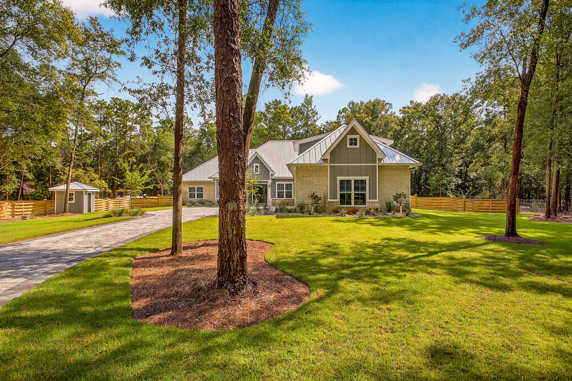 Suburban home with a green lawn, tall trees, and a driveway under a bright blue sky