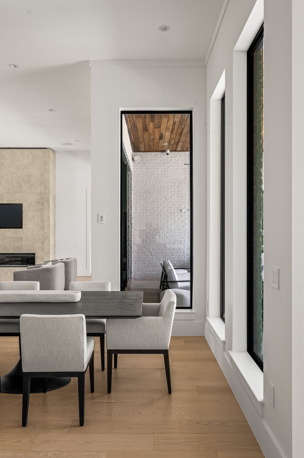 Modern living room with gray seating, wood floor, and tall windows overlooking a courtyard.
