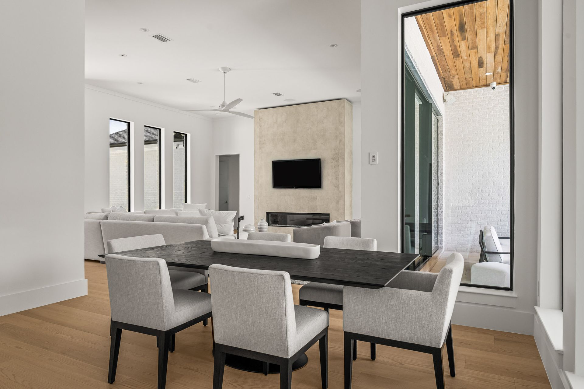 Modern dining room with a long table, gray chairs, wall-mounted TV, and bright patio doors