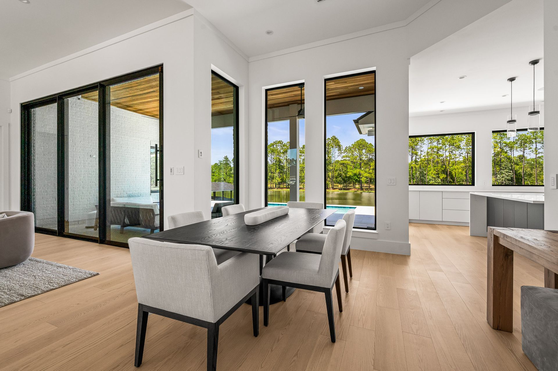Modern open-plan living room and dining area with large windows, light wood floors, and gray chairs