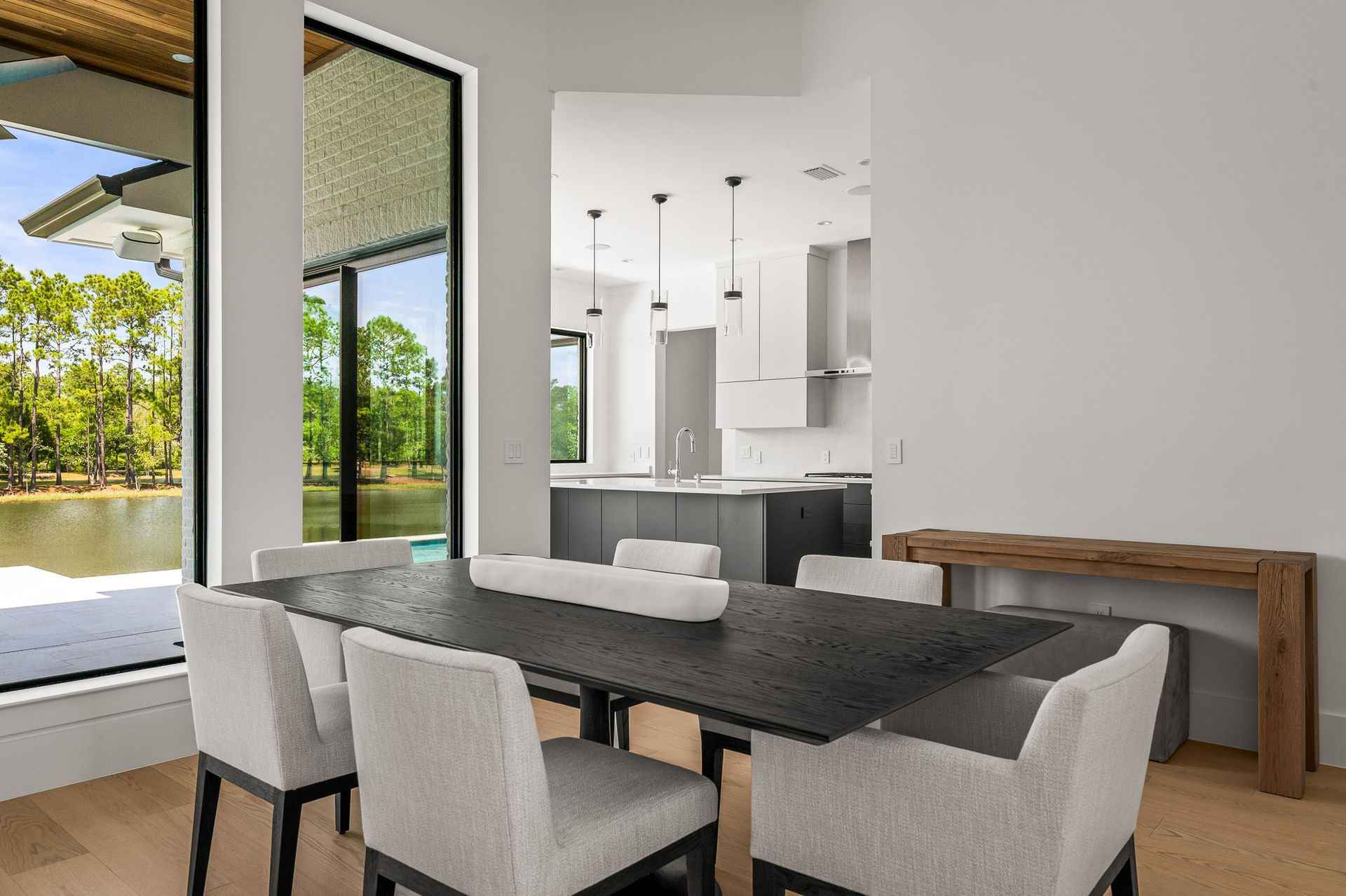 Modern dining area with black table, white chairs, and open kitchen beside large glass doors.