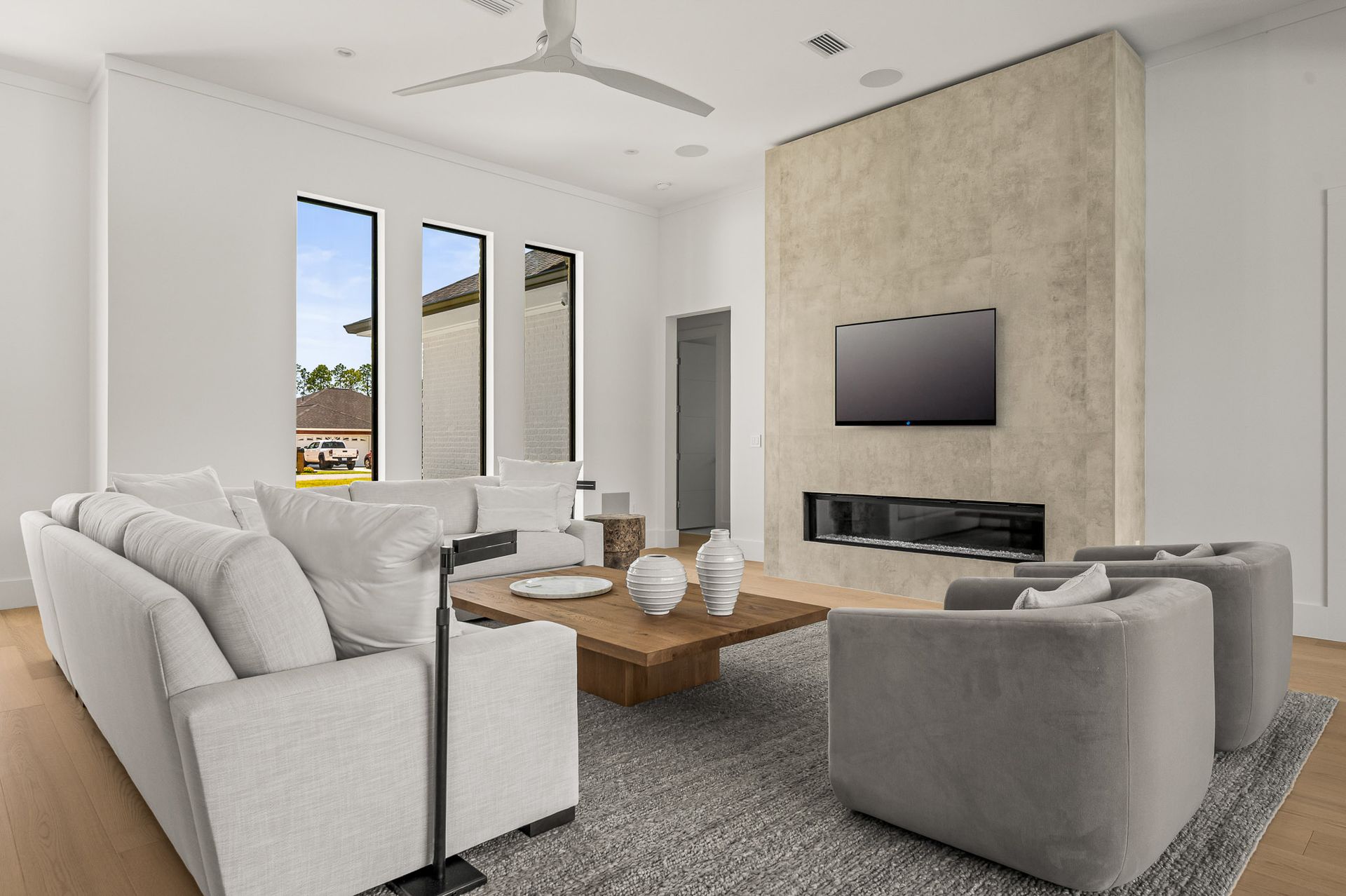 Modern living room with white and gray sofas, wood coffee table, wall-mounted TV, and large windows