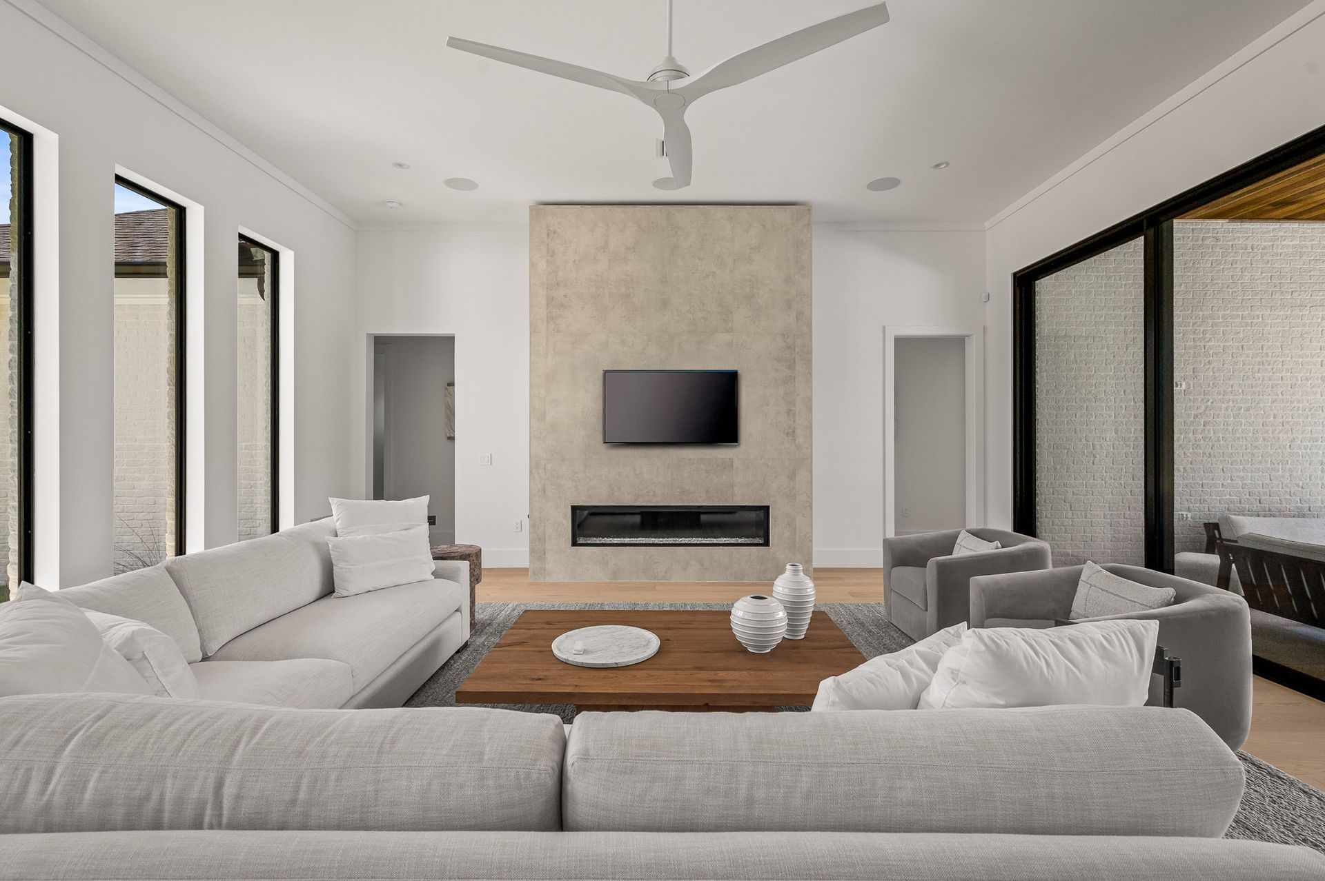 Modern living room with white sofas, wood coffee table, wall-mounted TV, and ceiling fan