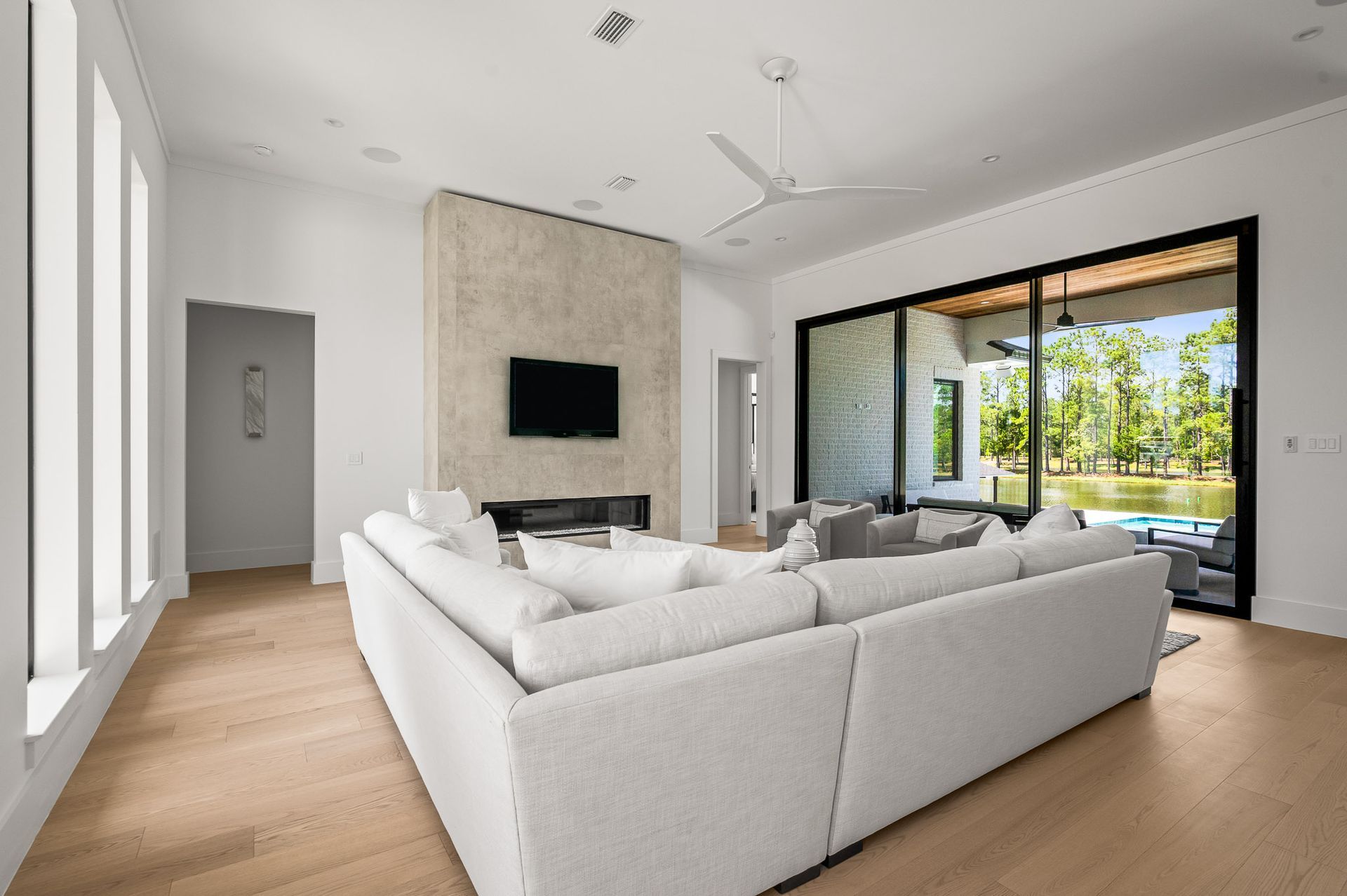 Modern living room with white sectional sofa, wall-mounted TV, and large sliding glass doors to a patio