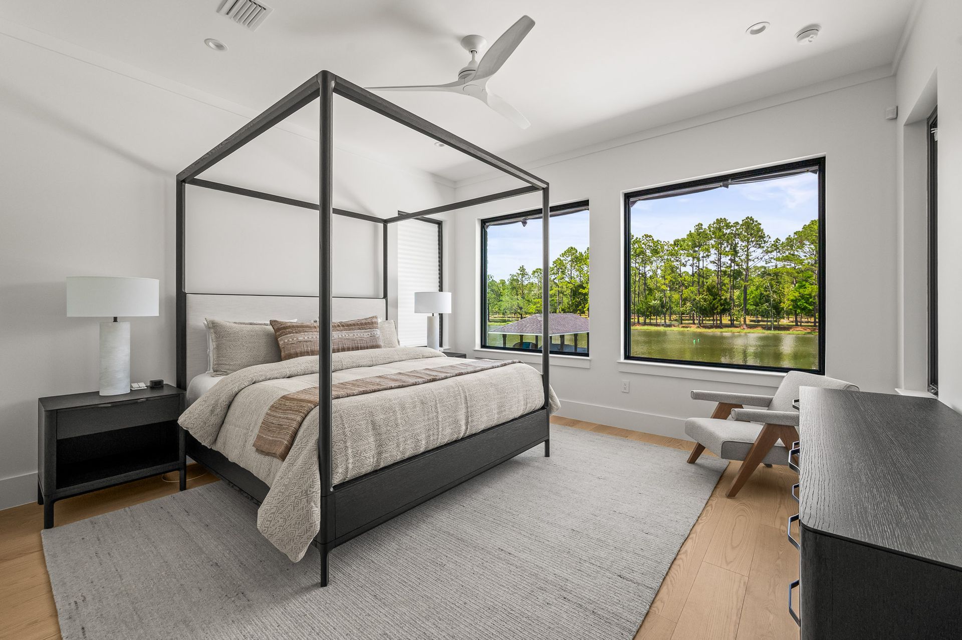 Modern bedroom with a four-poster bed, large window, and lake view