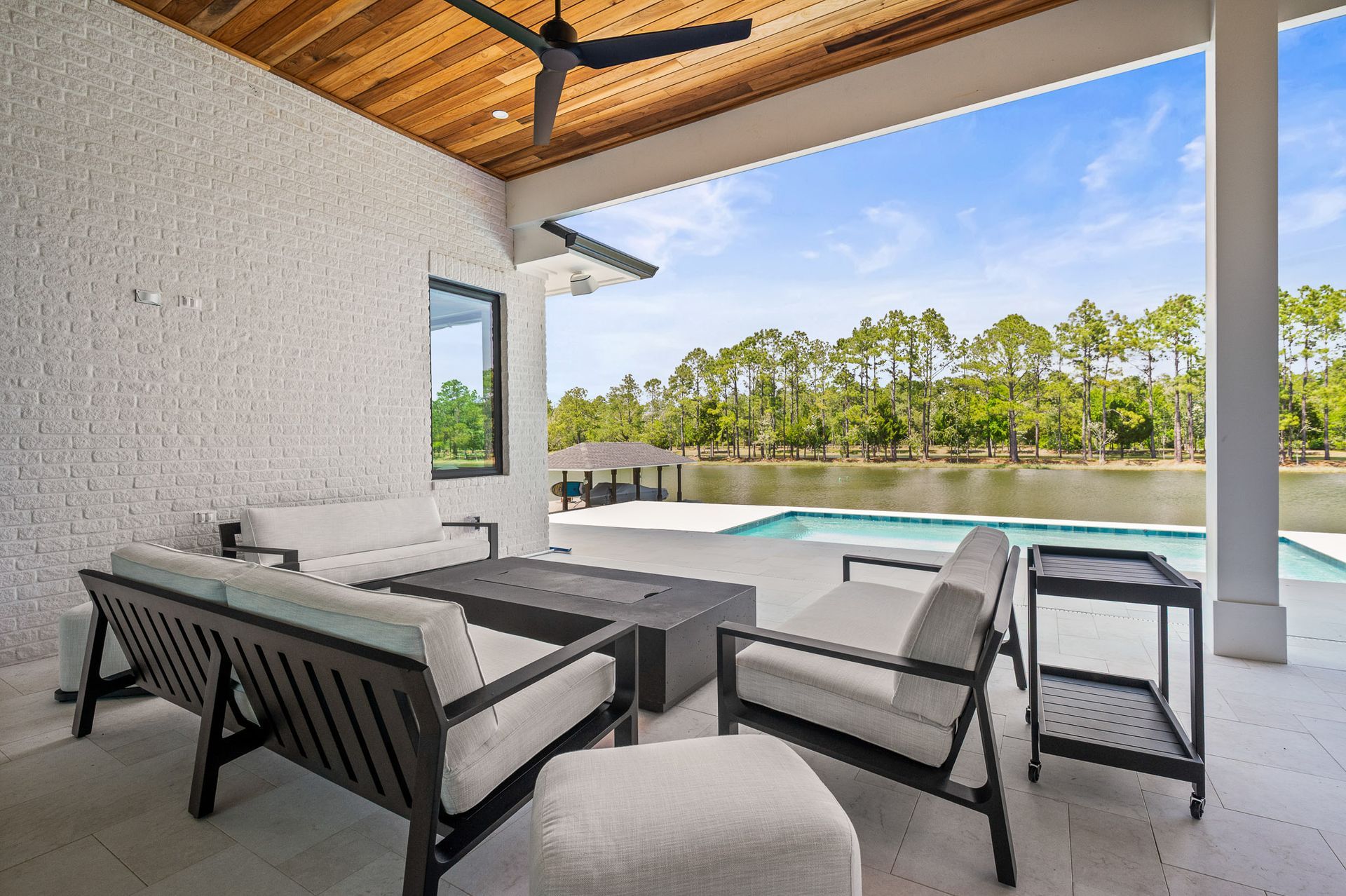 Covered patio with gray seating, pool, and trees beyond the deck