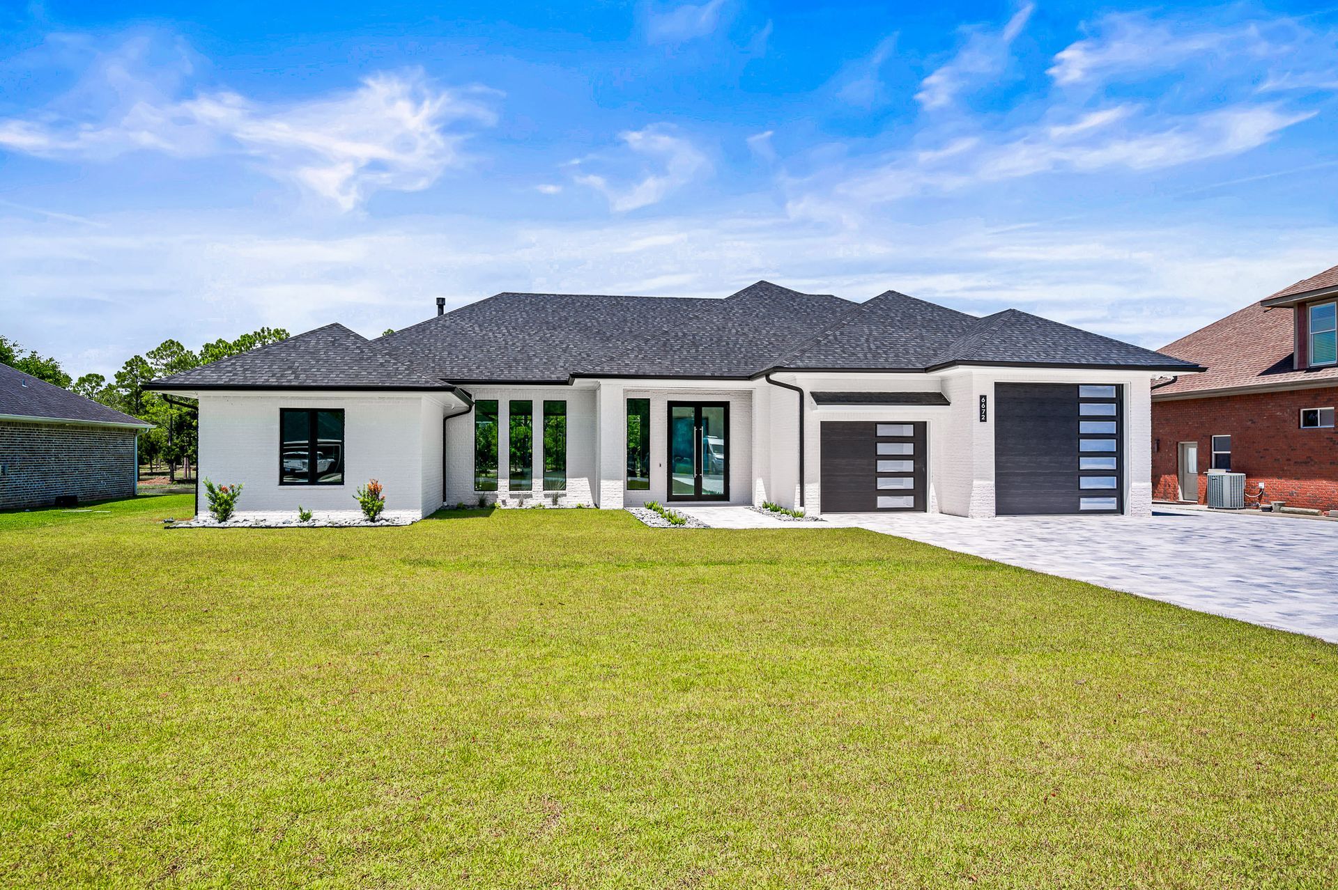 Single-story modern white house with gray roof and a large green lawn under a blue sky