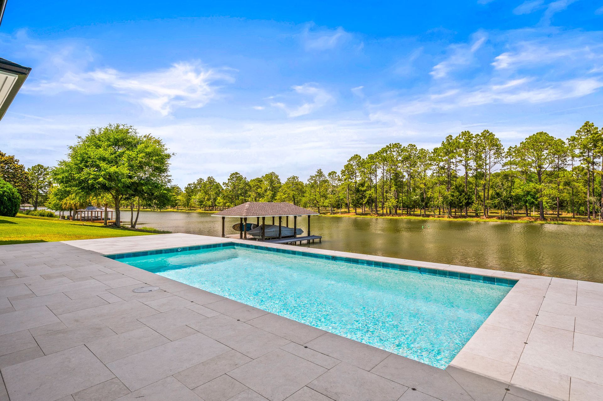 Modern backyard pool with turquoise water, stone patio, and trees under a blue sky