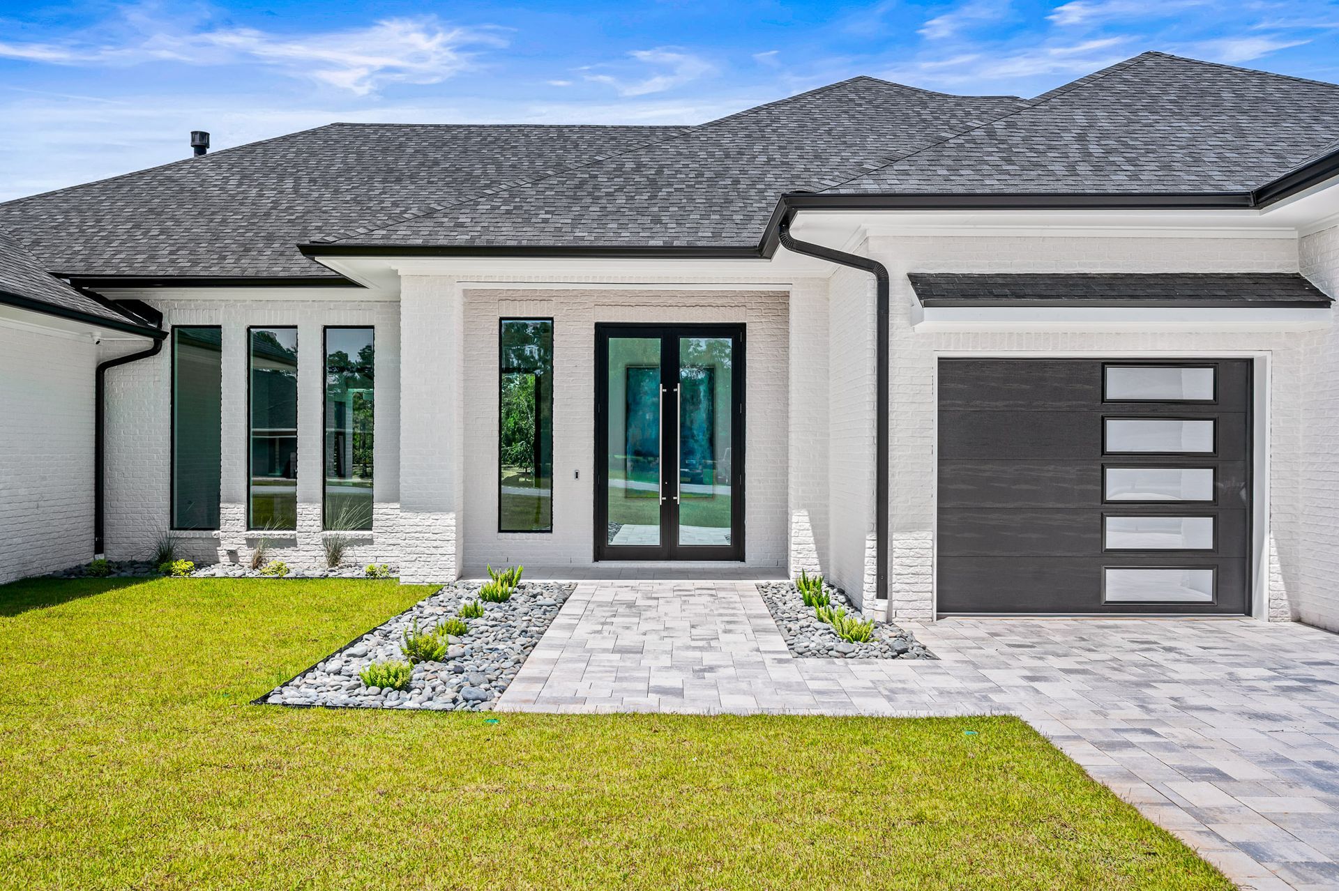 Modern white stucco house with gray roof, front lawn, stone walkway, and single-car garage