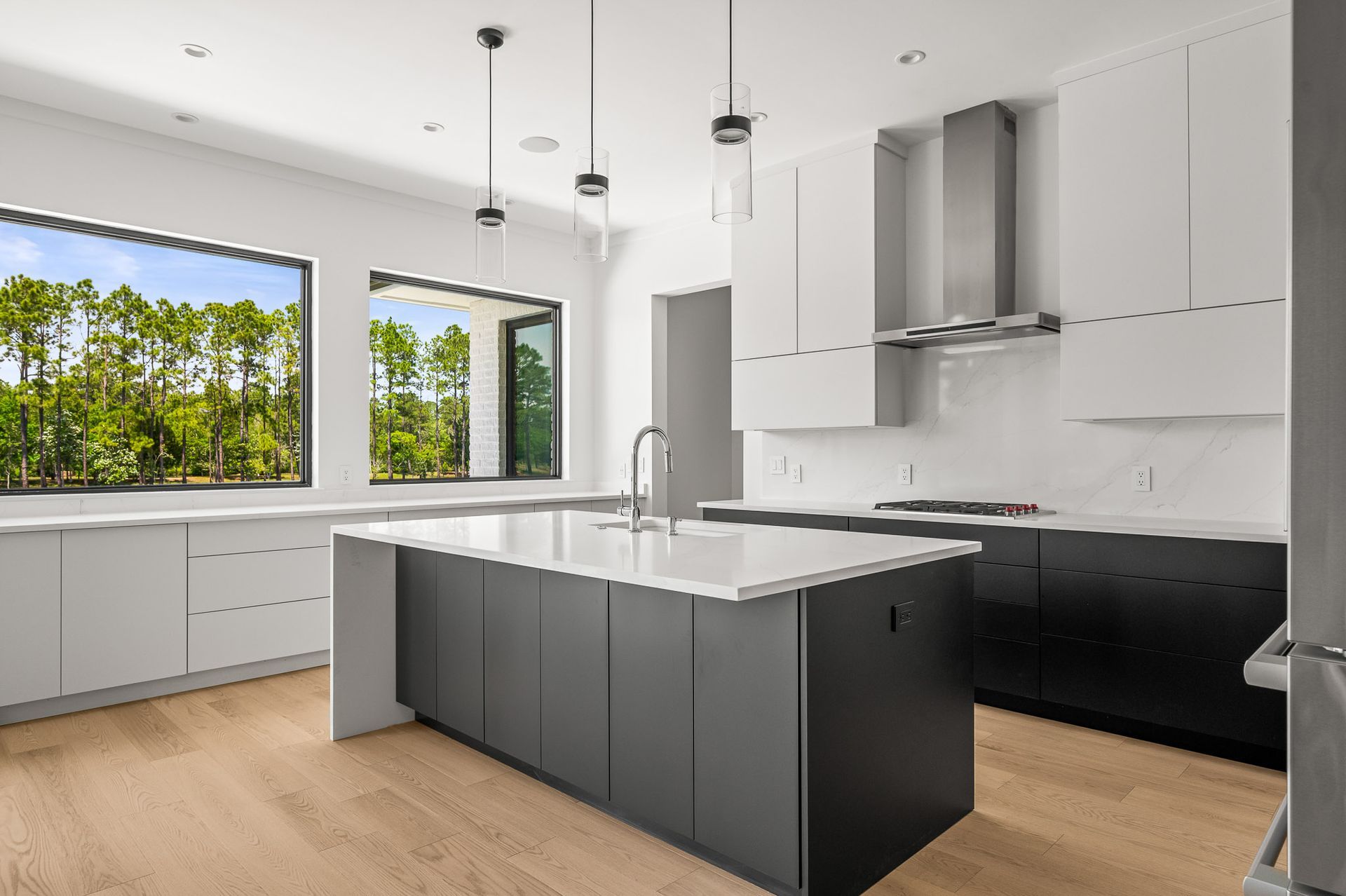 Modern white kitchen with gray island, black lower cabinets, and large windows overlooking trees