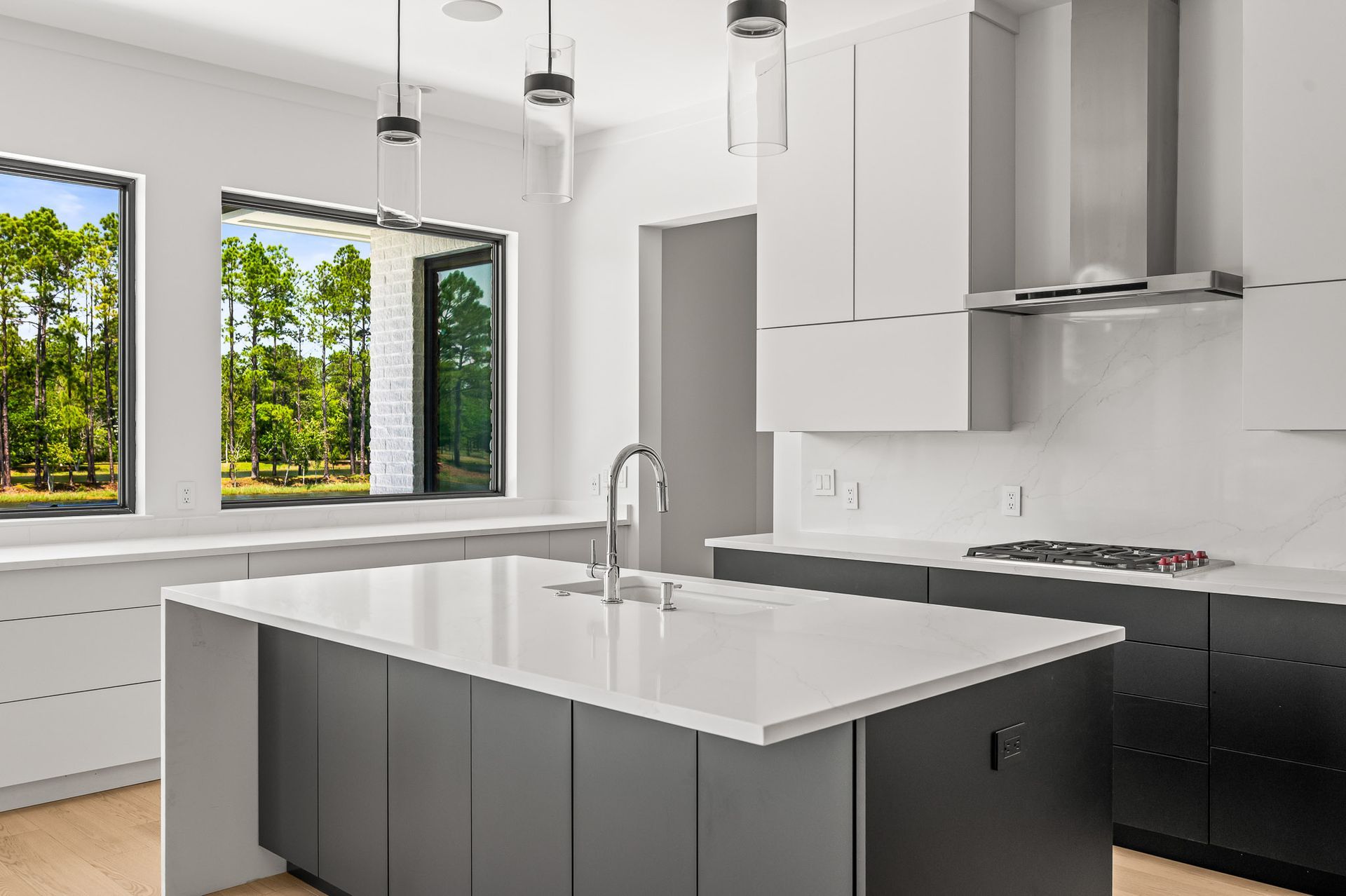 Modern kitchen with white cabinets, dark island, pendant lights, and large windows overlooking greenery