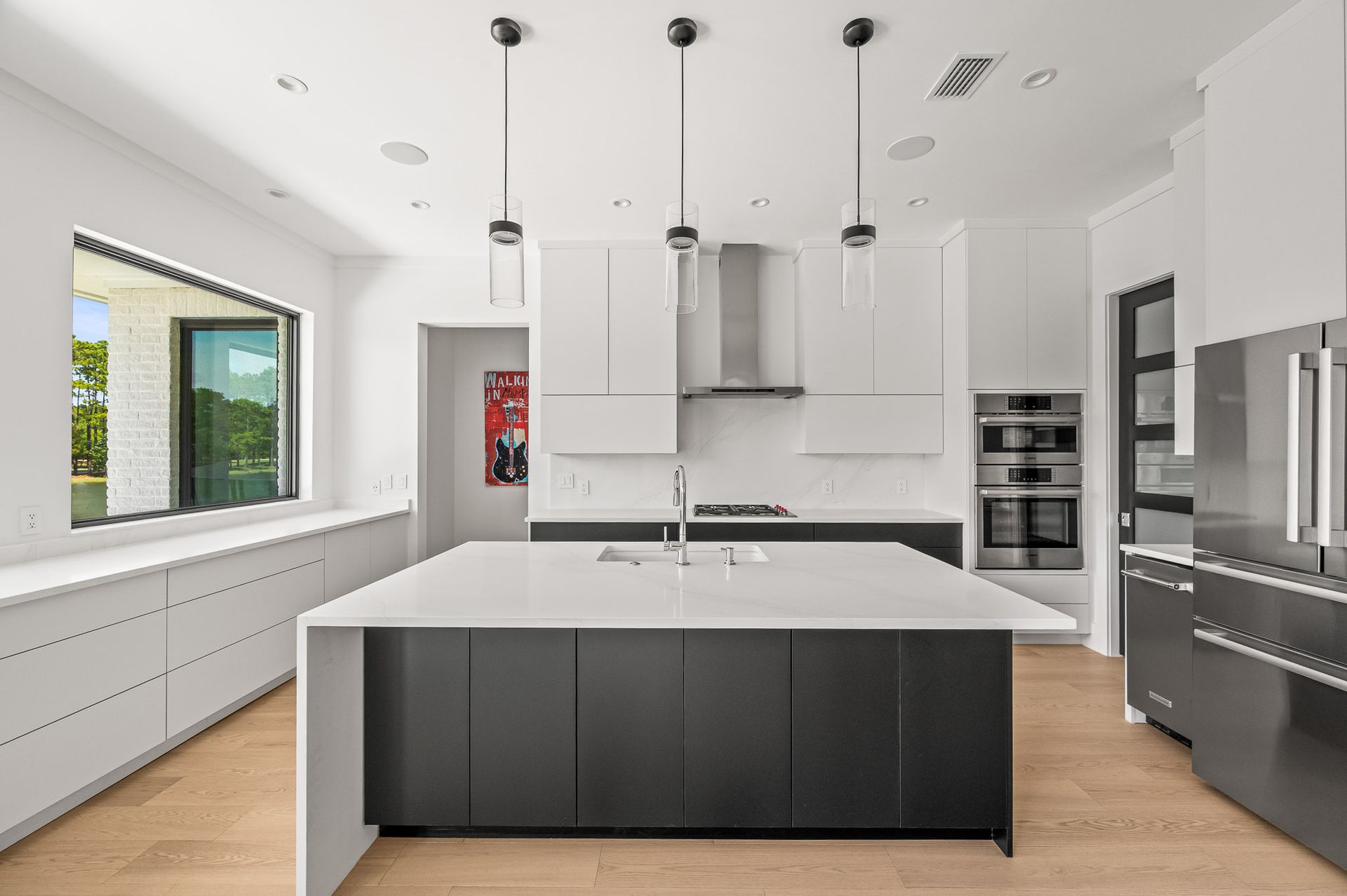 Modern white kitchen with black island, stainless appliances, and large windows