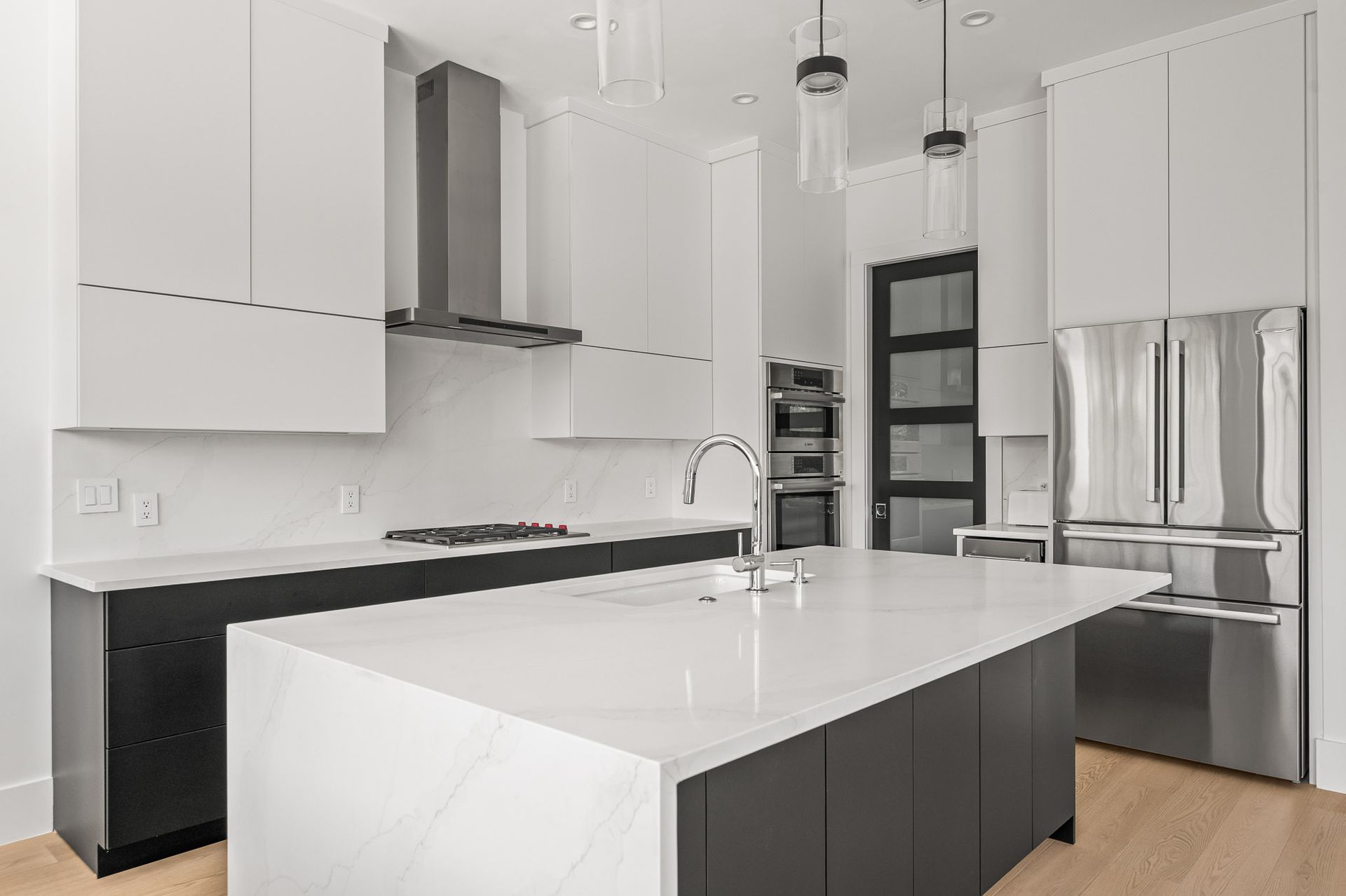 Modern white kitchen with a large island, stainless steel appliances, and dark lower cabinets