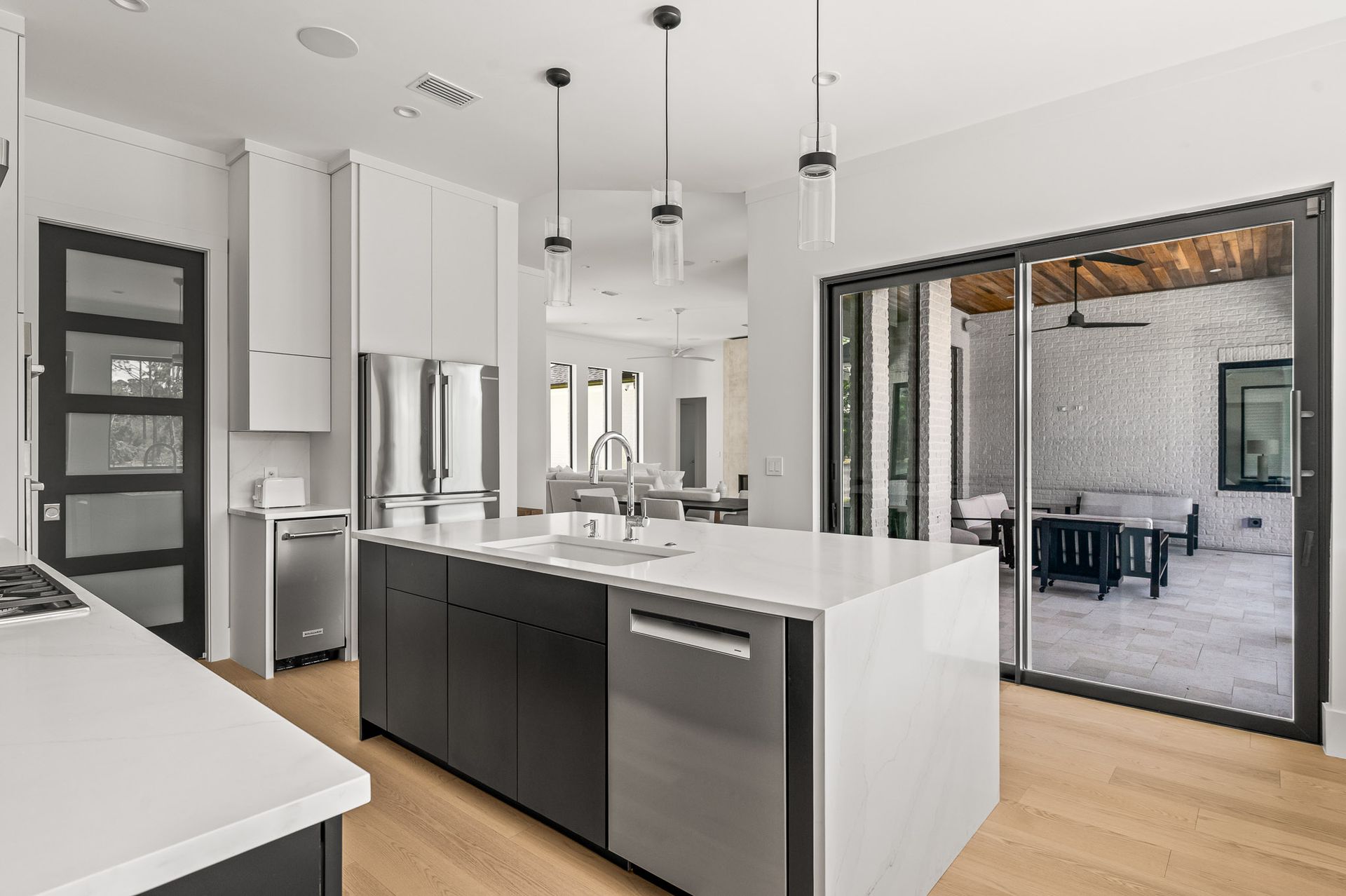 Modern open-plan kitchen with white island, black cabinets, stainless appliances, and sliding doors to a patio