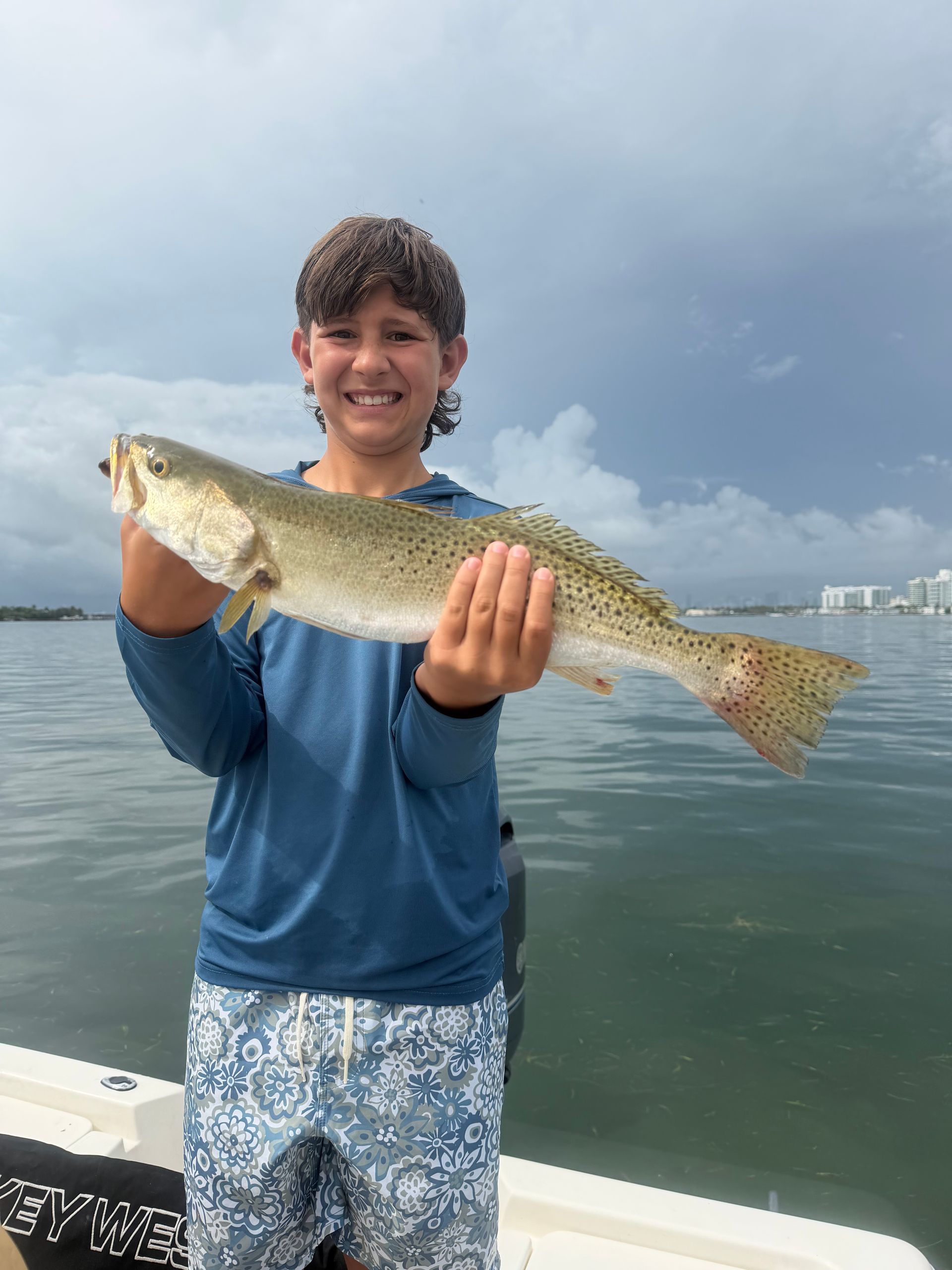 Person holding a large fish on a boat, with calm water and cloudy sky in the background