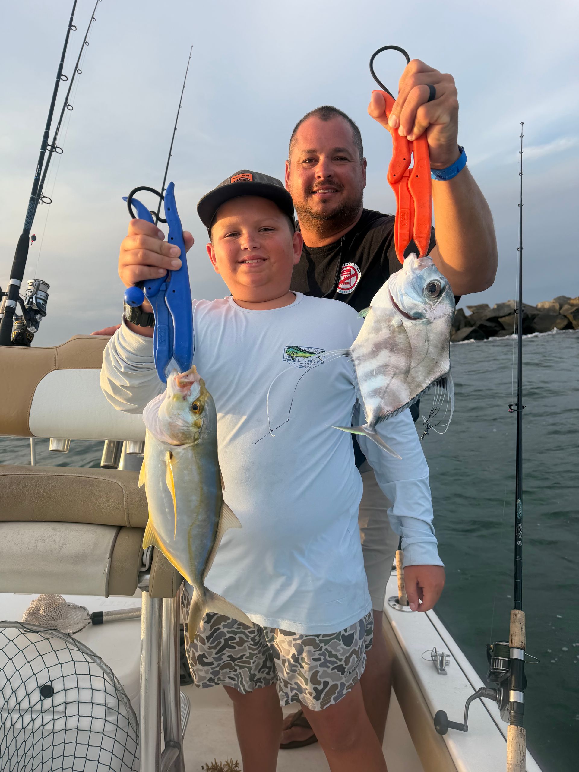 Two people on a boat holding up two large fish by their hooks.