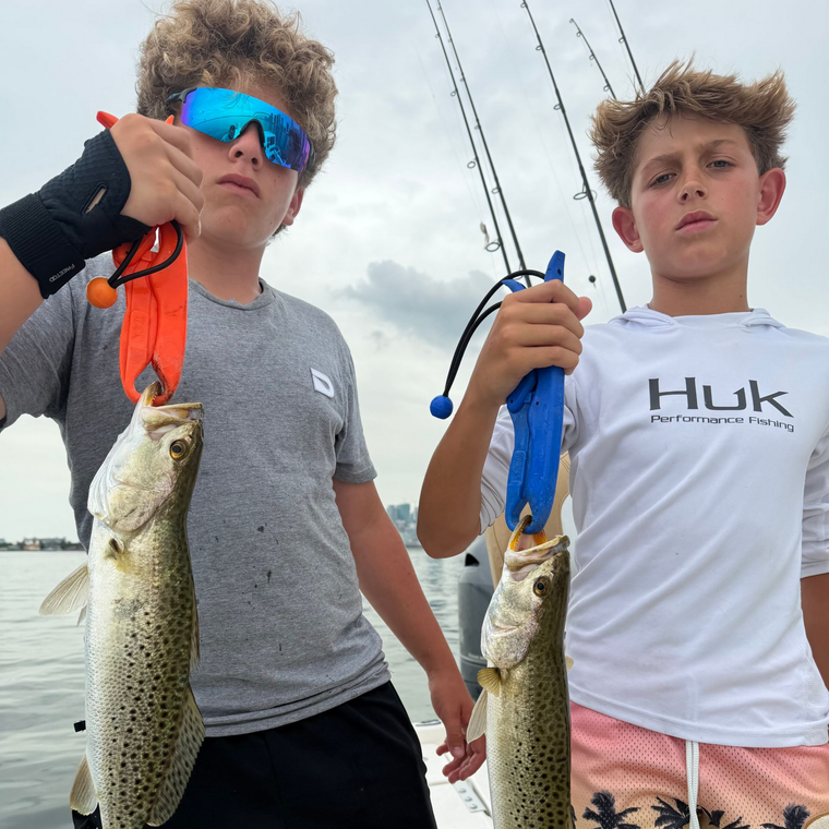 Two people holding up fishing rods and fish on a boat, wearing sunglasses and casual shirts.