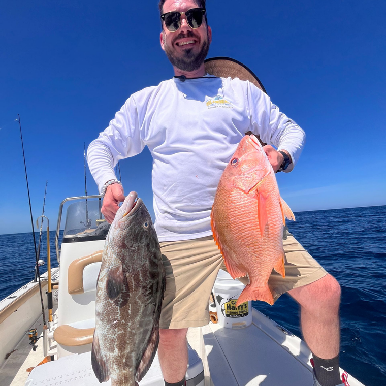 Man on a boat holding two large fish on a sunny day at sea.