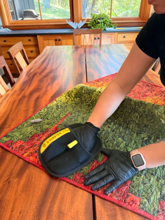 Person using a lint roller on a green and red table runner on a wooden dining table