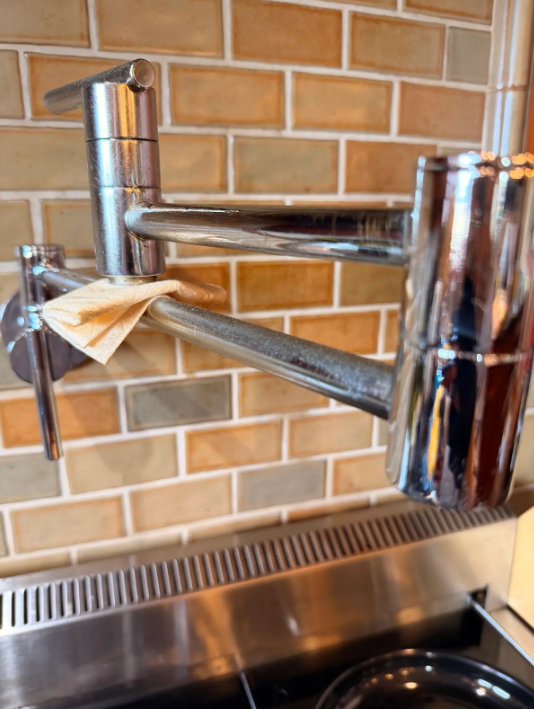 Chrome wall-mounted adjustable shelf bracket over a stainless steel sink against a brick-tile wall