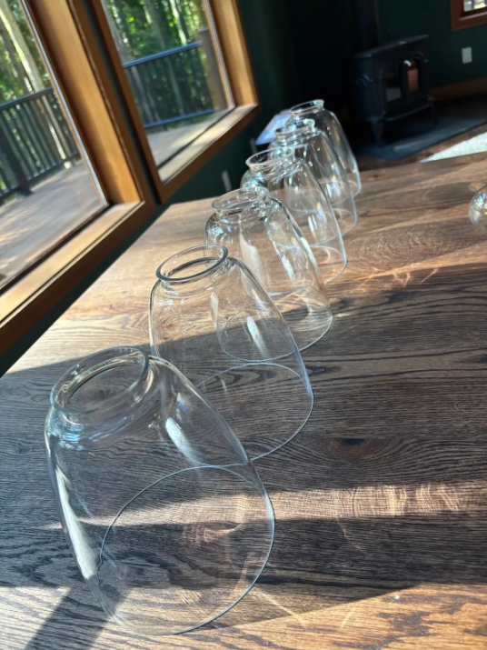 Upside-down clear glasses lined on a sunlit wooden table by windows