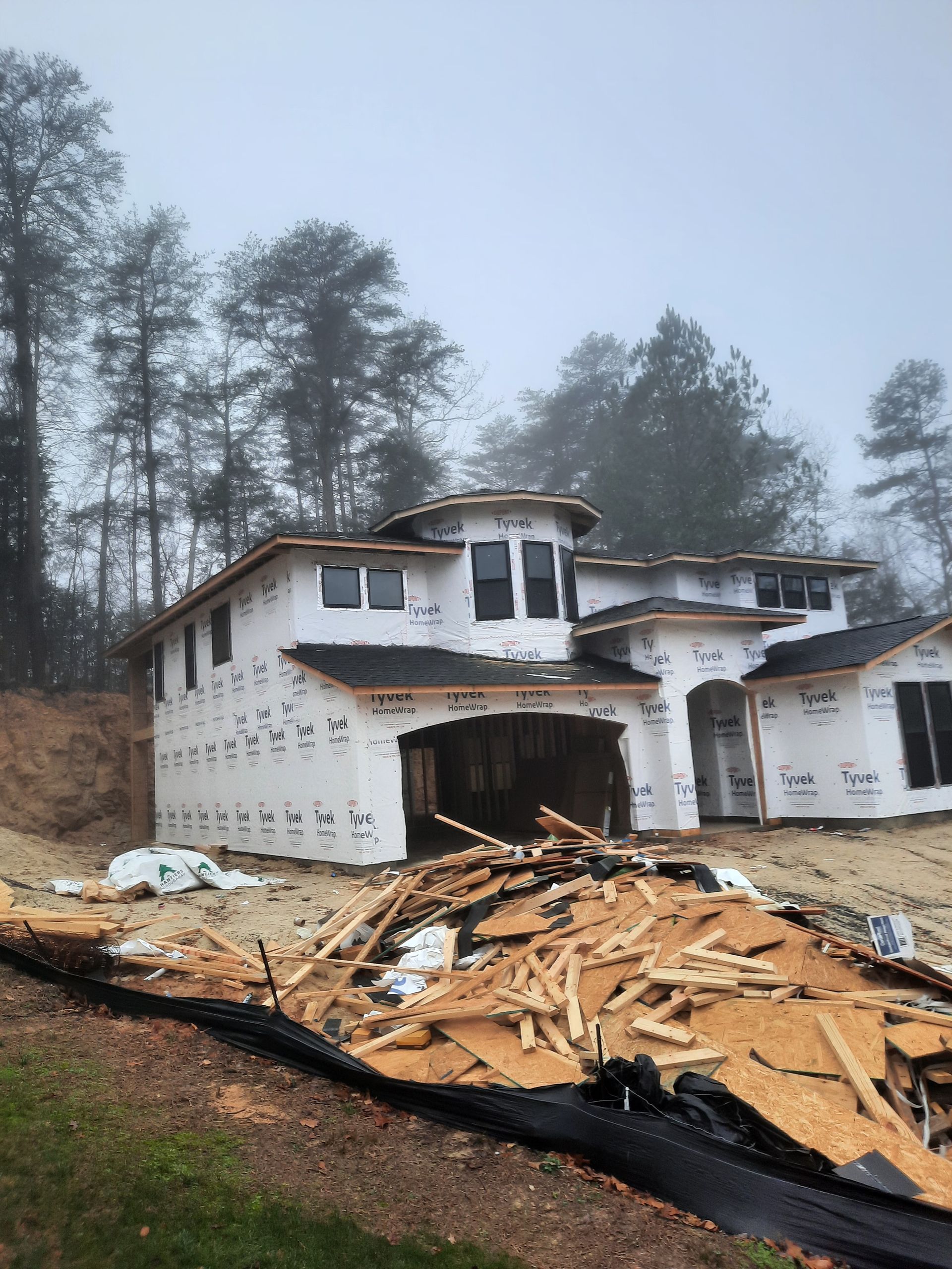 A house under construction with a pile of wood in front of it.