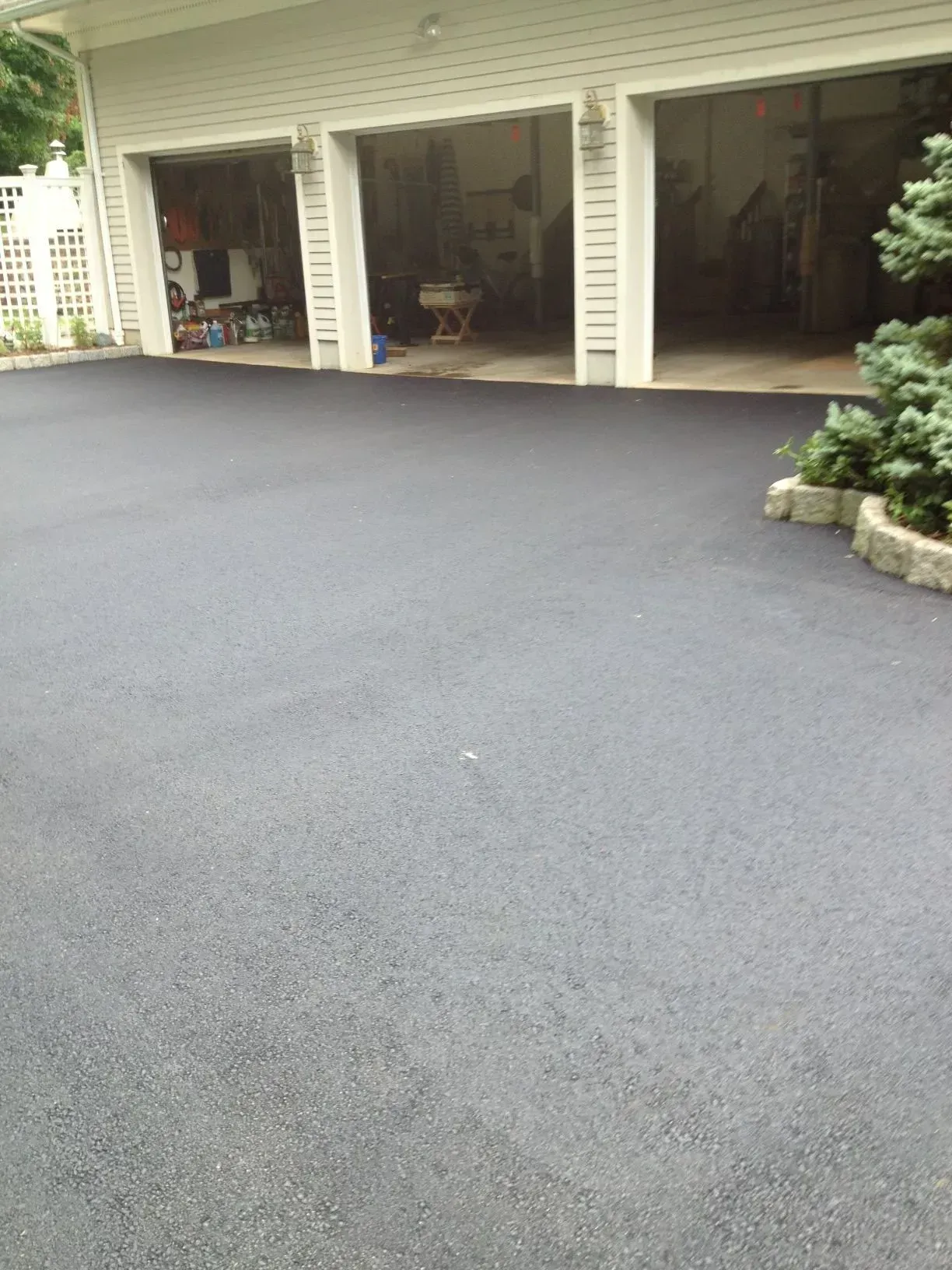 Newly paved asphalt driveway in front of a three-car garage with open doors.