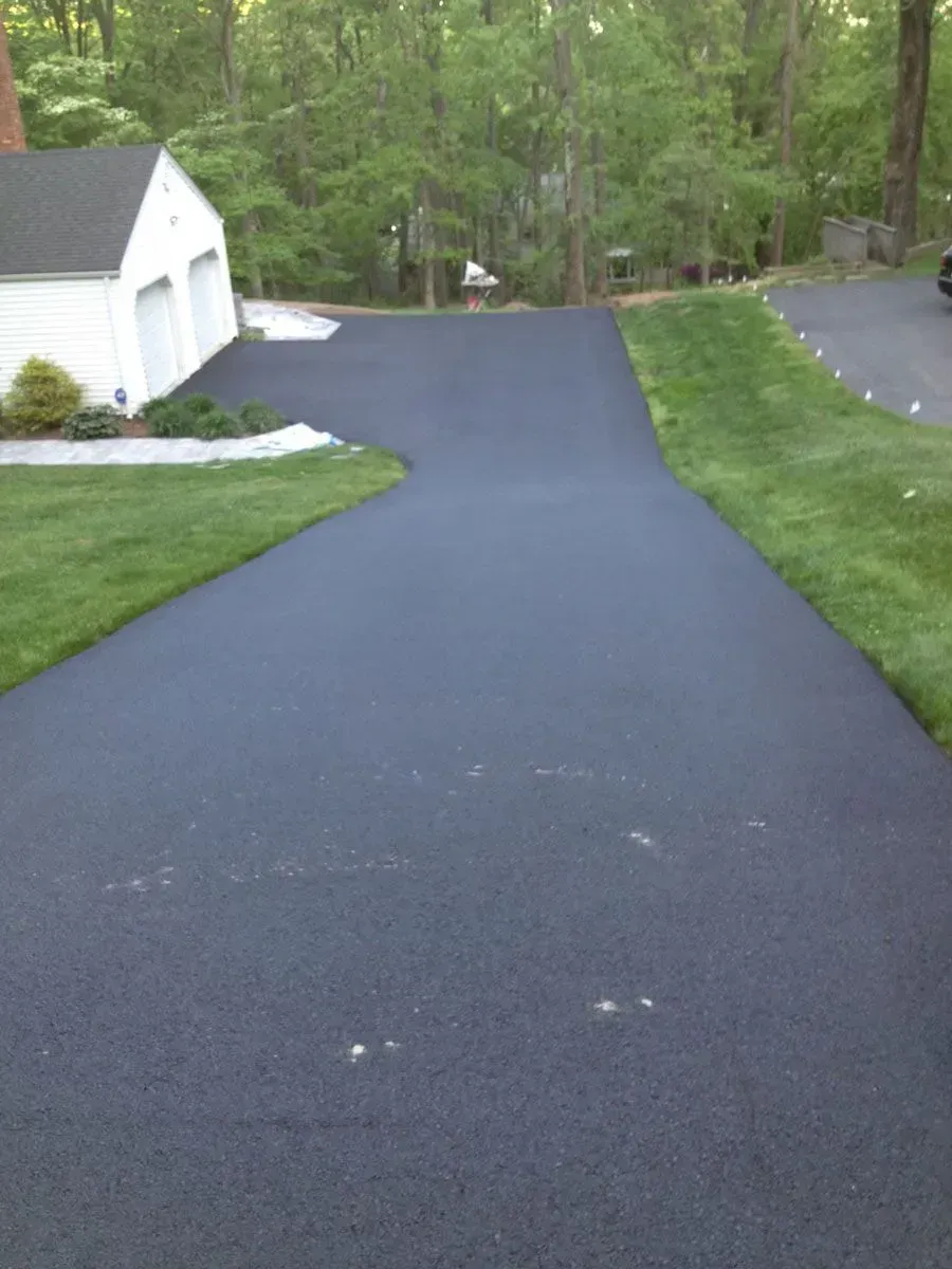 A newly paved asphalt driveway curves toward a garage.