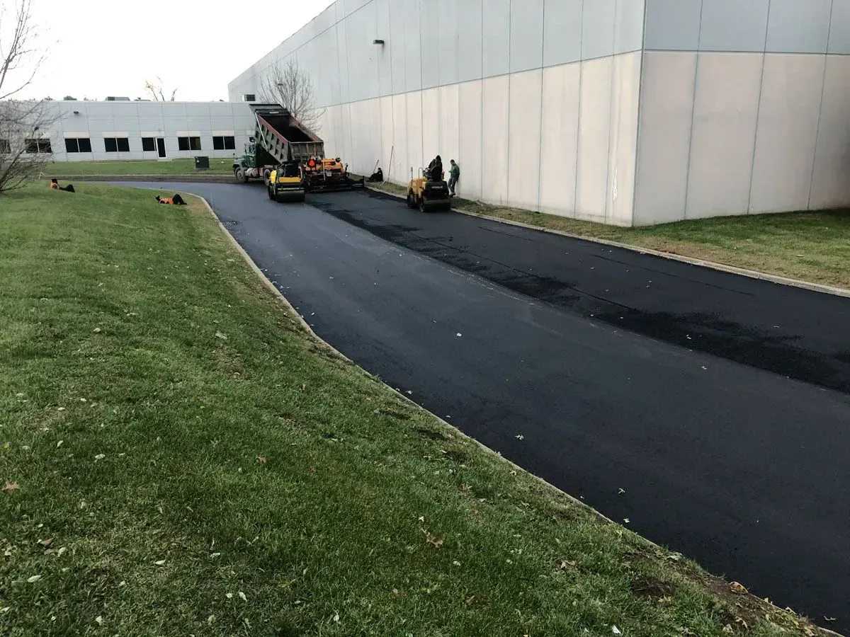 Asphalt paving in progress near a light industrial building.