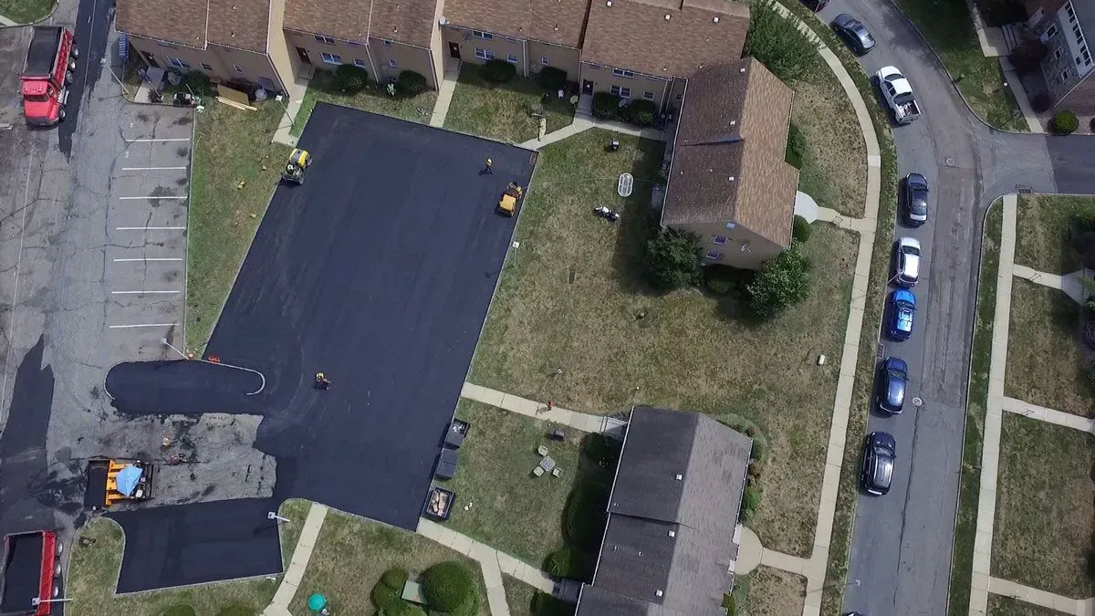 Aerial view of asphalt paving work in progress next to apartment buildings and parked cars.