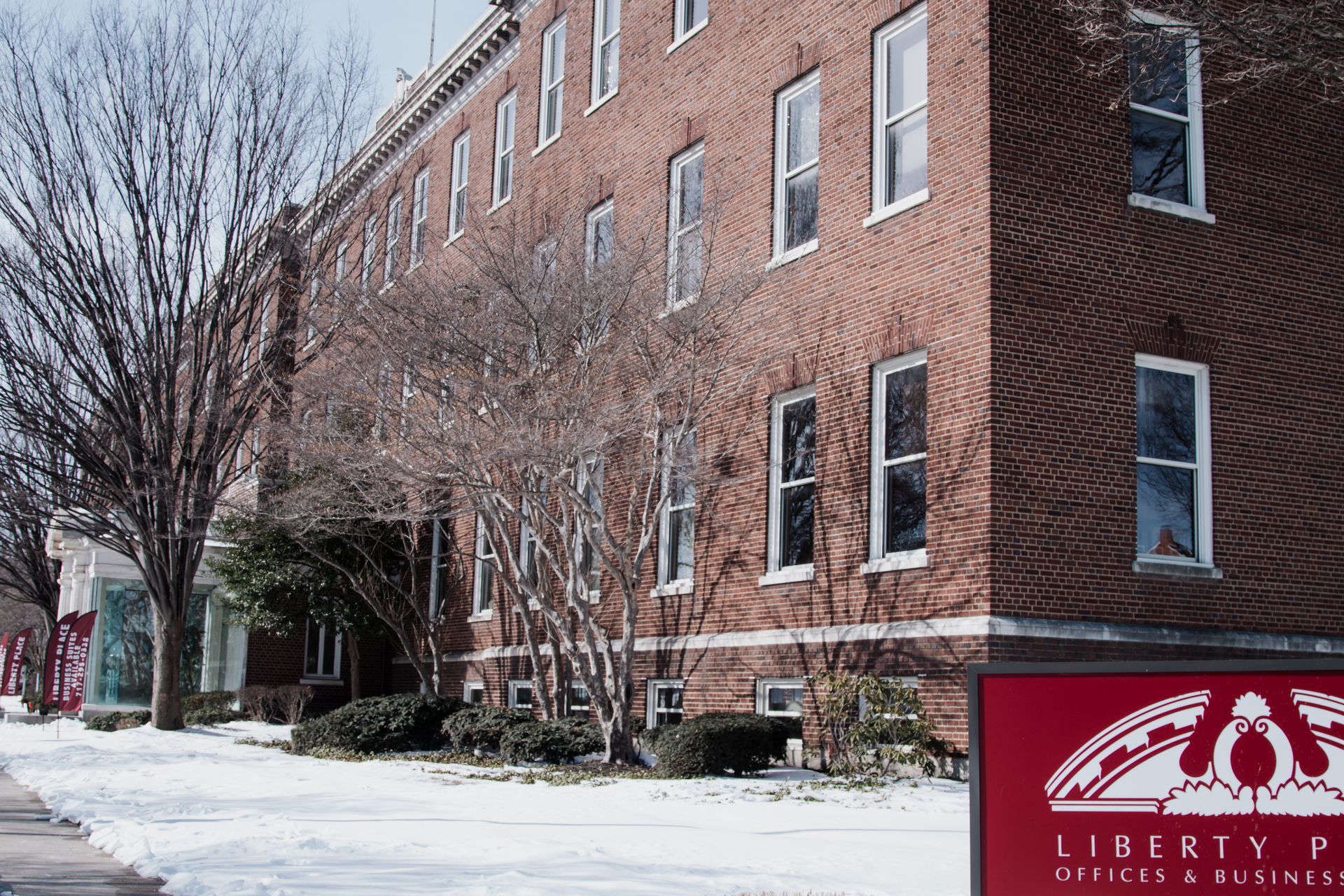 Snowy street beside a red brick building with bare trees and a Liberty sign