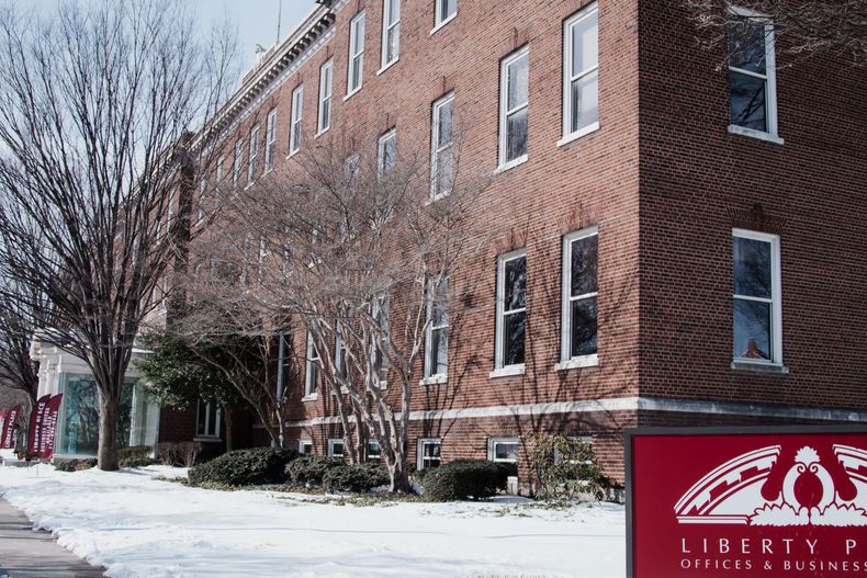 Snowy street beside a red brick building with bare trees and a Liberty sign