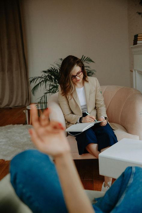 Woman taking notes on a couch in a cozy living room while another person gestures in the foreground