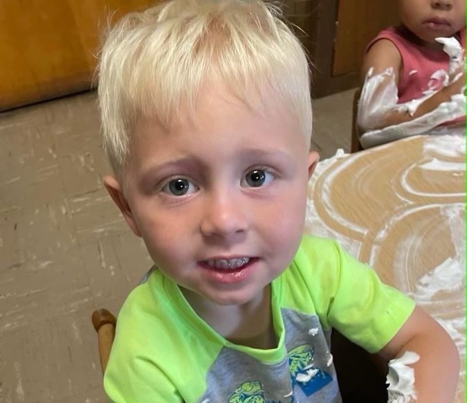 A young boy in a green shirt is sitting at a table covered in foam.