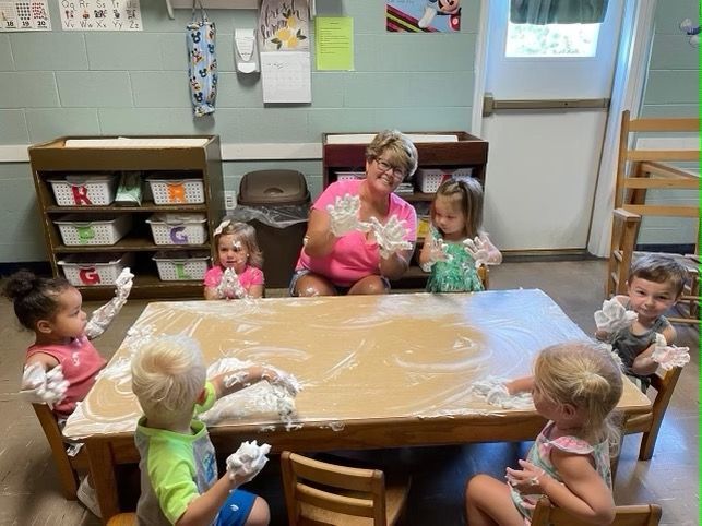 A group of children are sitting around a table playing with soap bubbles.