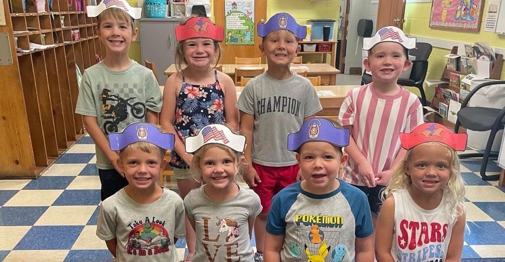 A group of children wearing pirate hats are posing for a picture in a classroom.