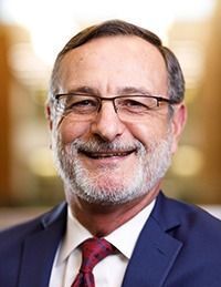 A man with a beard and glasses is wearing a suit and tie and smiling.