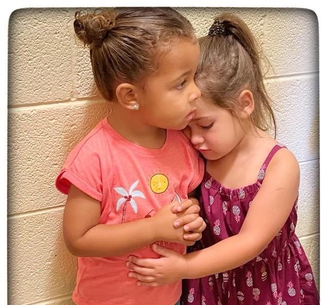 Two little girls hugging each other in front of a brick wall