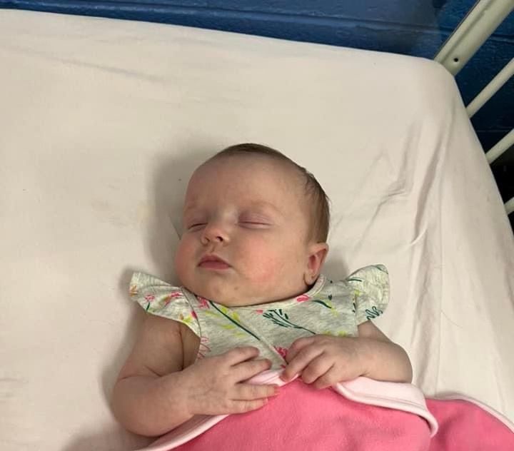 A baby is sleeping on a bed with a pink blanket