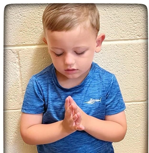 A young boy in a blue shirt is praying