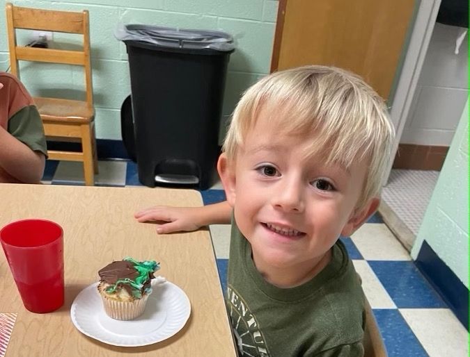 A young boy sits at a table with a cupcake on a plate