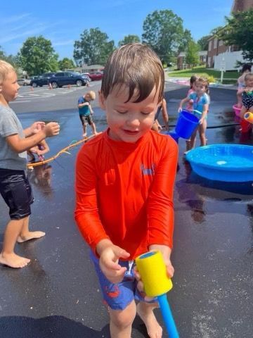 A young boy in a red shirt is playing with water in a parking lot.