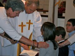 People at a church service. A child is blessed by an officiant, others watch.