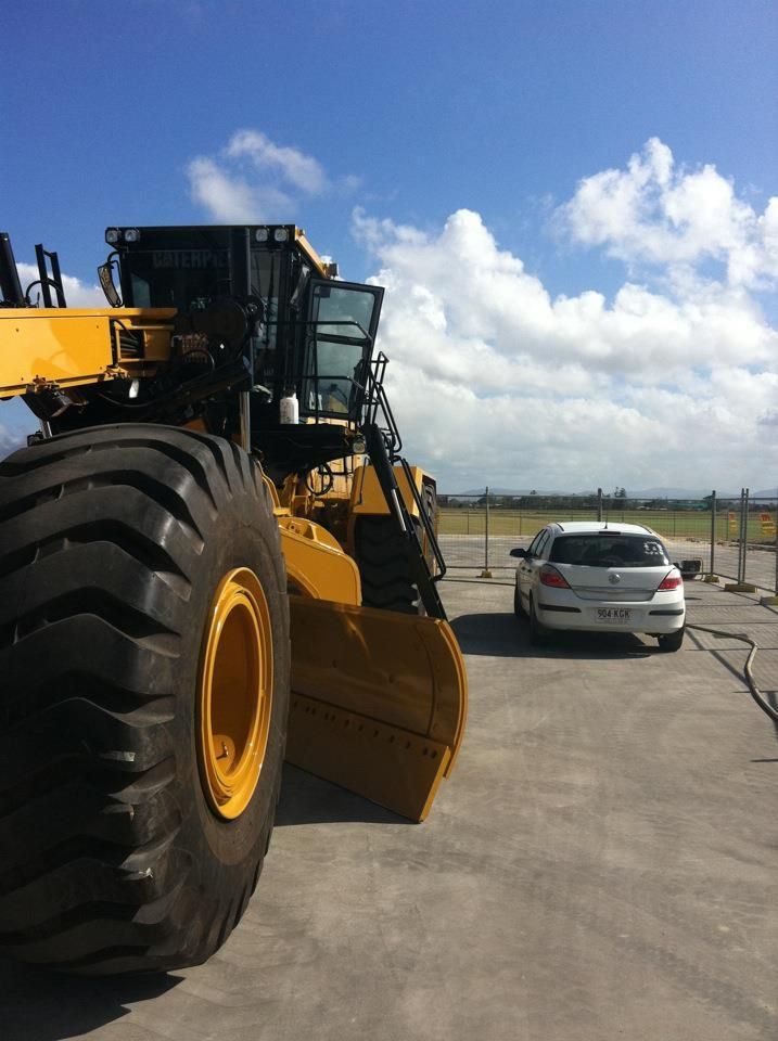 A Large Yellow Bulldozer Is Parked Next to A White Car — Epic Window Tinting in Glenella, QLD