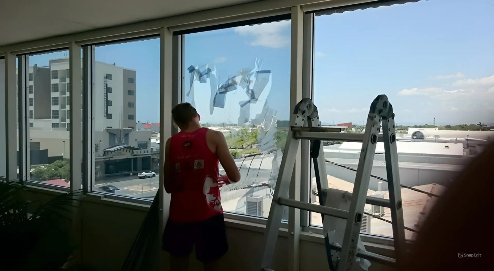 A Man in A Red Tank Top Is Cleaning a Window — Epic Window Tinting in Glenella, QLD