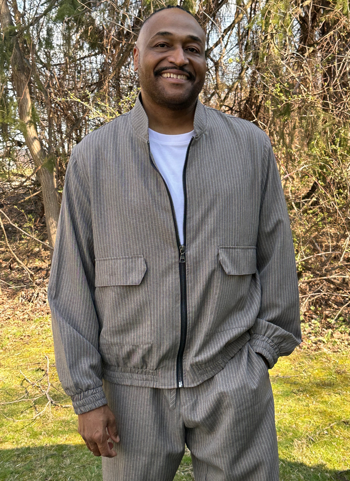 Reverend Jermaine T. Bracy smiliing while standing outdoors in a gray patterned jacket and pants with a white shirt.