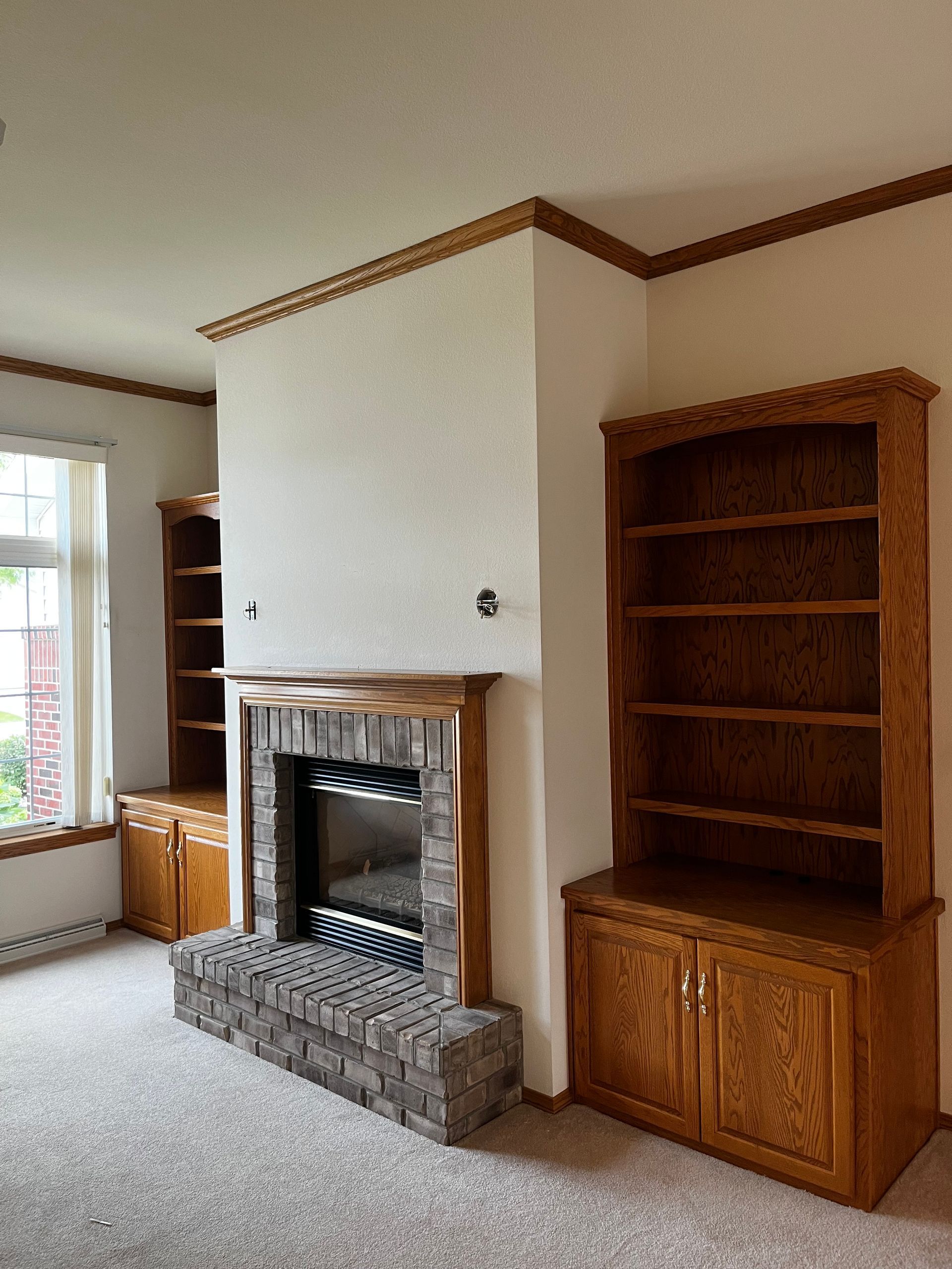 An empty living room with a fireplace and shelves