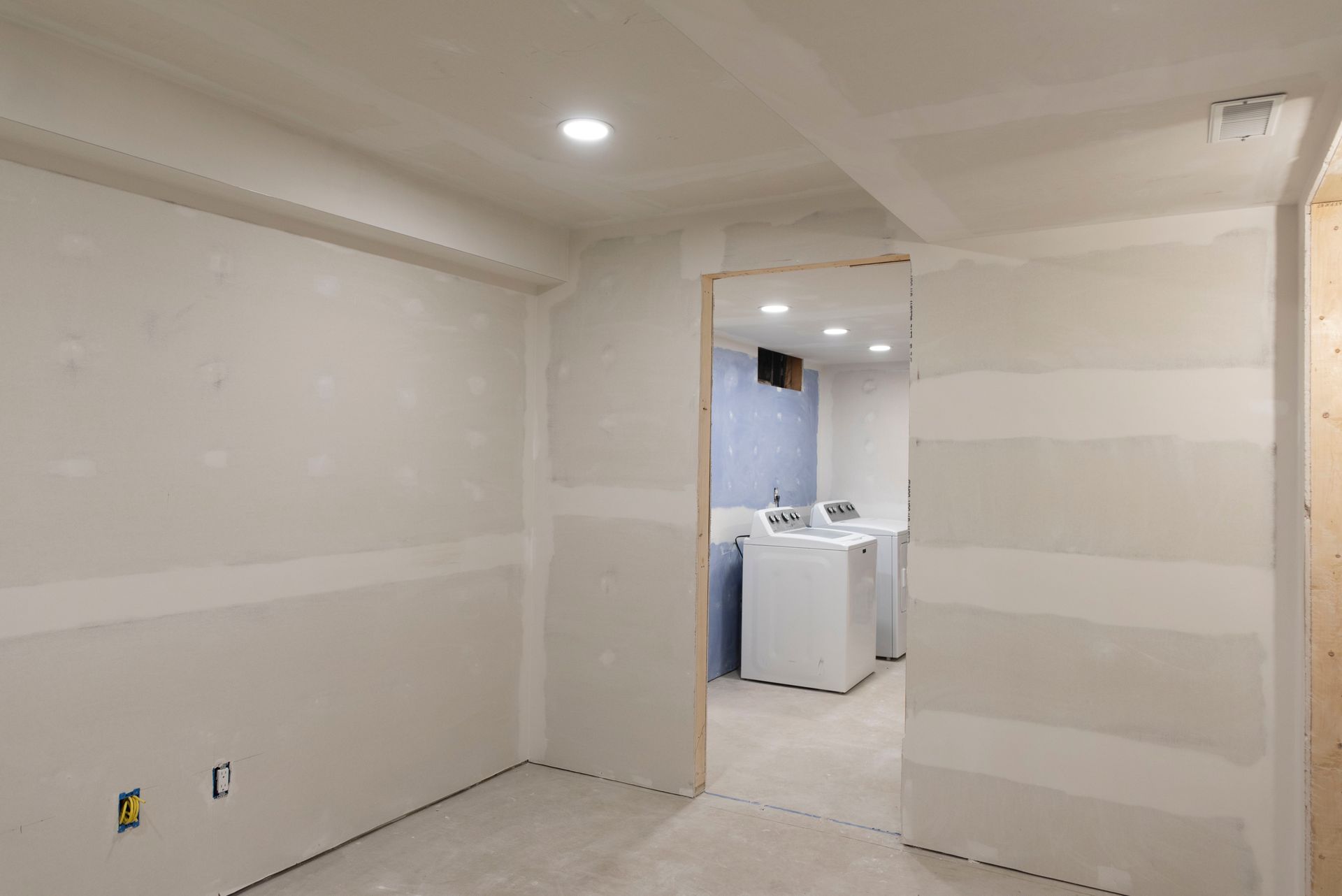 Interior room under construction, with drywall walls and doorway leading to laundry appliances.