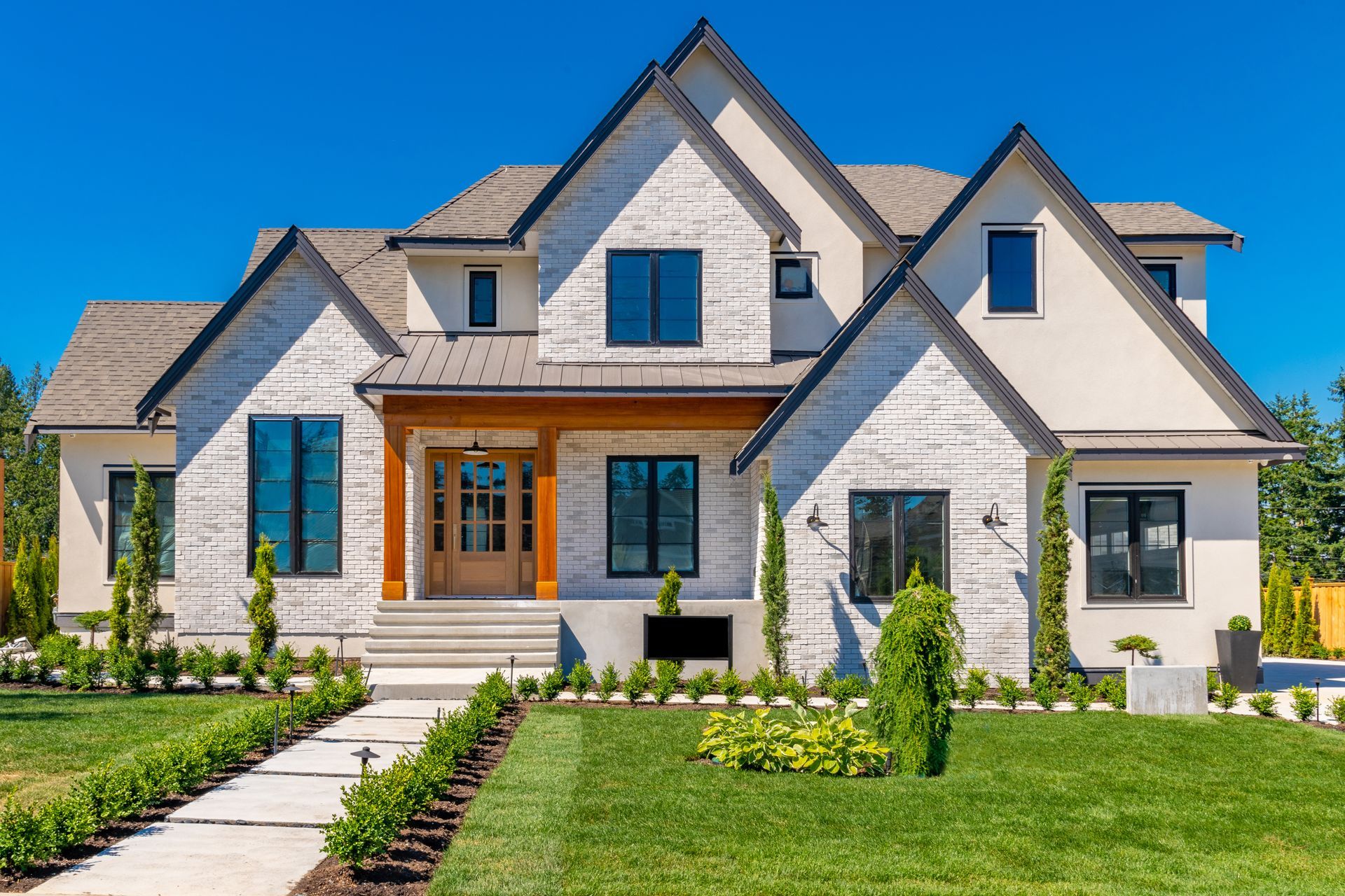 Two-story house with white brick exterior, dark windows, and manicured lawn on a sunny day.