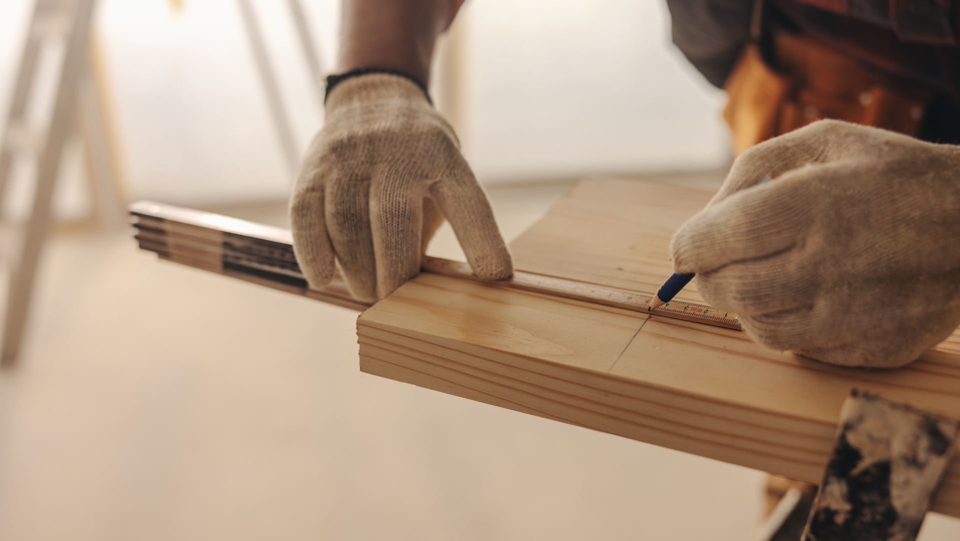 Person in gloves using a ruler to measure and mark a wooden board with a pencil.